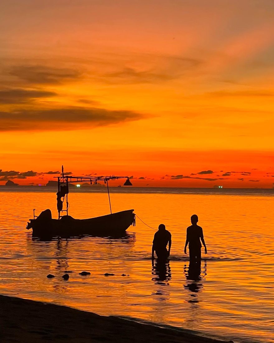 Two people wading near a fishing boat at sunset